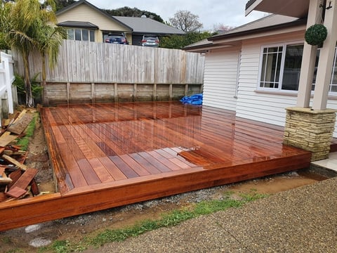 Newly constructed reddish-brown wooden deck in backyard with houses and fence visible in background