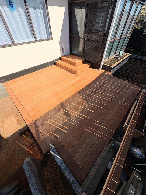 Exterior patio area with new wooden deck platform partially installed next to a modern house with glass doors and sliding windows