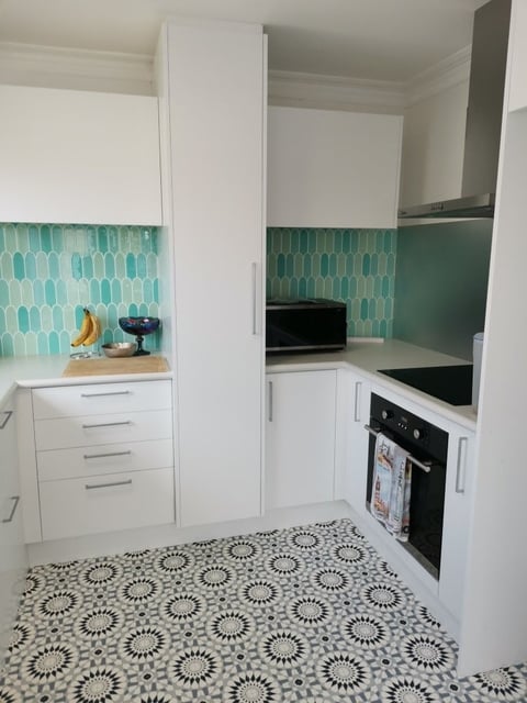 Modern compact kitchen with white cabinets, turquoise tile backsplash, black appliances, and geometric patterned floor tiles