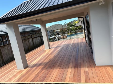 Modern covered patio with wooden deck flooring, white columns, and metal roof overlooking a pool area