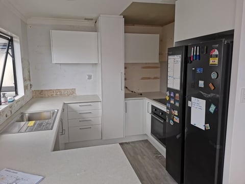 Modern kitchen under renovation with white cabinetry, black refrigerator, open layout, and beige countertops