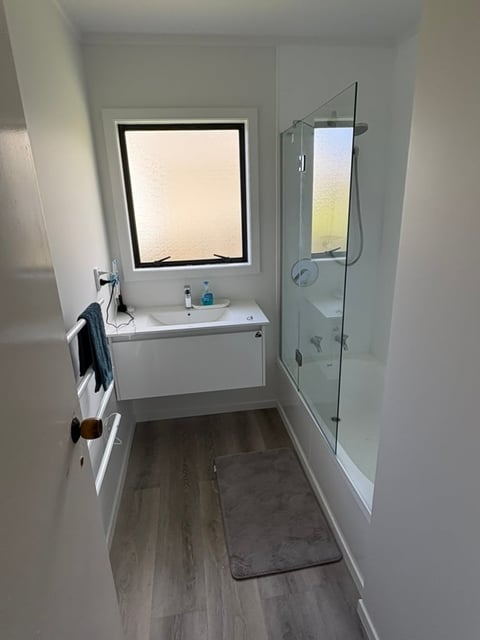 Modern bathroom with white vanity, glass shower enclosure, frosted window, and wood-effect flooring