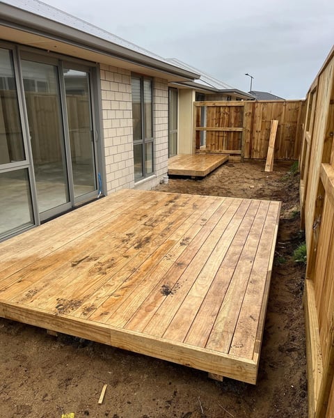 Newly constructed wooden deck attached to a modern house with large windows and wooden fencing on sides