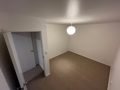 Empty room with gray carpet, white walls, ceiling light, and open doorway on the left side