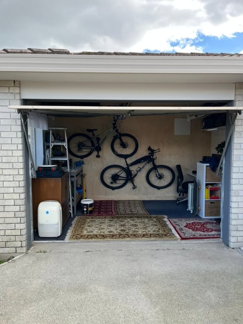 Open garage with two bicycles mounted on wall, white water heater, storage shelves, and ornamental rugs on floor