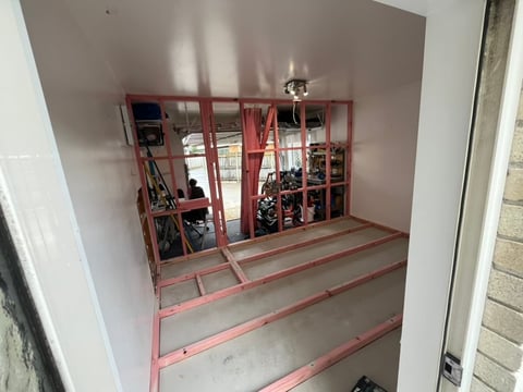 Interior room under construction with red metal framing on floor and walls, showing exposed framework and stored materials