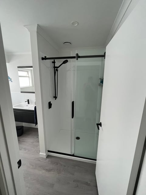 Modern bathroom with glass sliding shower door, black hardware, white tile walls, and gray wood-look flooring