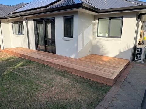 Modern house with timber deck extension, white walls, metal roof, and manicured lawn with pavers