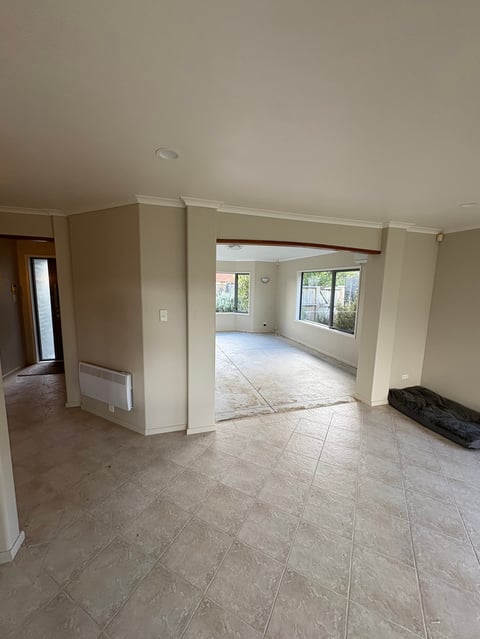 Empty modern living space with tile flooring, beige walls, and multiple windows providing natural light