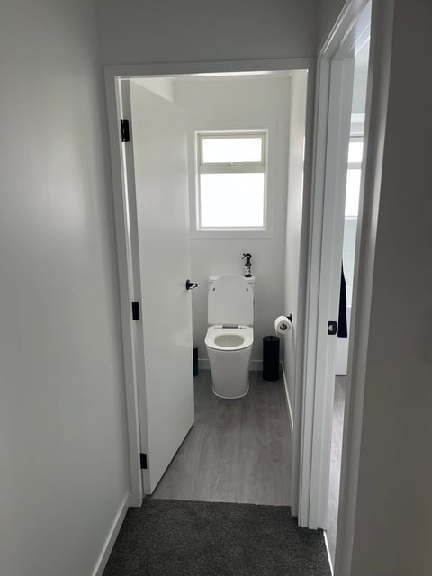 Modern bathroom interior viewed through open doorway, featuring toilet, window, and gray tile flooring