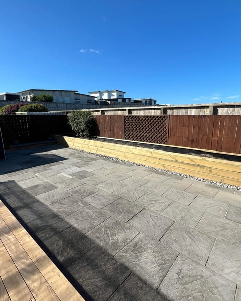 Rooftop patio with paved tiles, wooden fence, and city buildings visible against blue sky