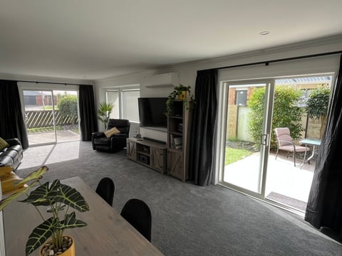 Modern open-plan living room with dining table, TV, black chairs, and glass doors opening to a garden patio