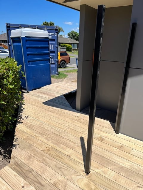 Wooden deck with metal support posts, blue portable toilet visible in background under sunny skies