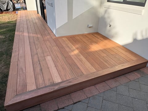 Wooden deck with warm brown tones extending from a modern white house with glass doors and landscaped grass