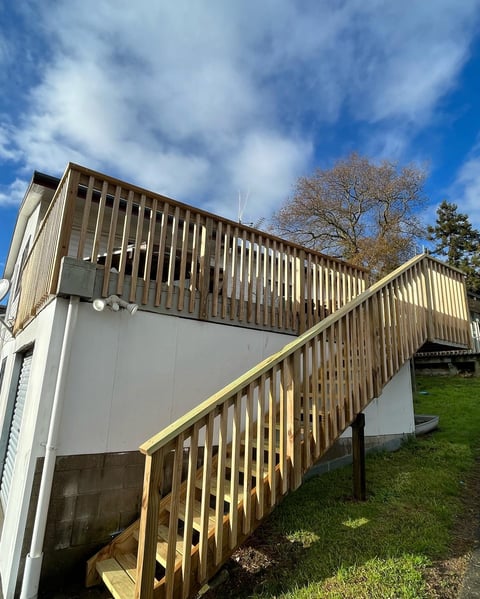 Modern wooden deck structure with metal railings attached to a white building under blue sky