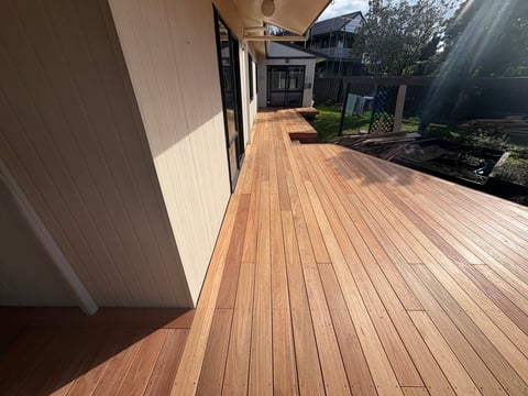 Long wooden deck with planked flooring extending between houses and outdoor space with landscaping