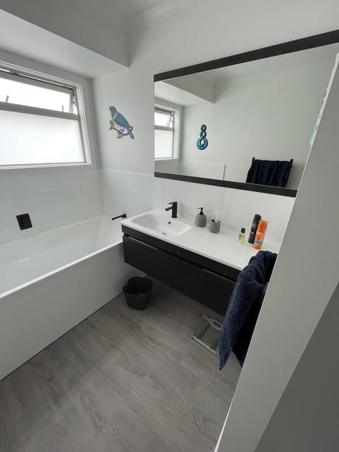 Modern bathroom with white walls, black and white vanity, large mirror, bathtub, and gray vinyl flooring