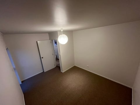 Empty basement room with white walls, dark concrete floor, round ceiling light, and blue tape marking on doorways