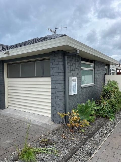 Modern garage with dark brick exterior, white trim, and horizontal siding door, featuring landscaping and paved driveway