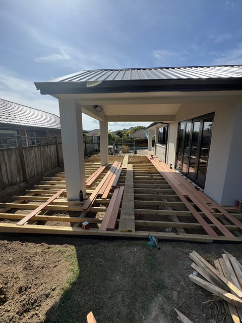 Construction of modern house extension with metal roof frame, wooden deck framing, and glass sliding doors under clear sky
