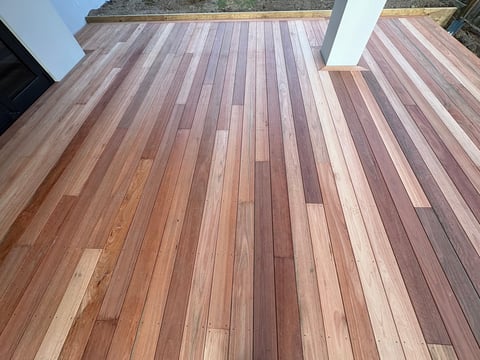 Wooden deck with varied brown and reddish planks arranged in a linear pattern, featuring a white support beam