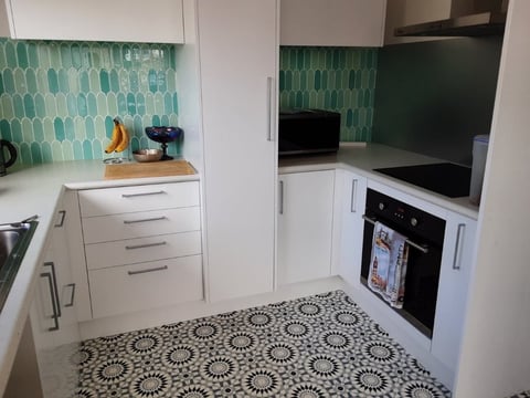 Modern kitchen with white cabinets, teal geometric backsplash tile, patterned floor, and built-in oven
