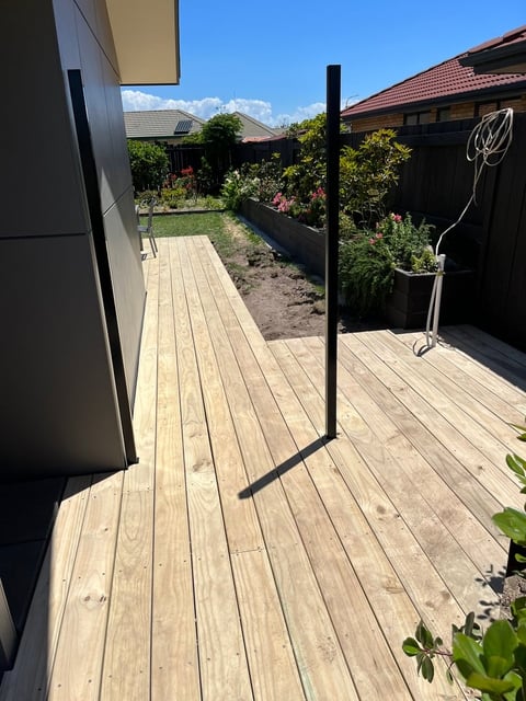 Wooden deck with black metal clothesline pole, surrounding garden beds with flowers and shrubs, houses visible in background