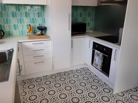 Modern kitchen with white cabinetry, teal geometric tile backsplash, built-in oven, and patterned black and white floor tiles