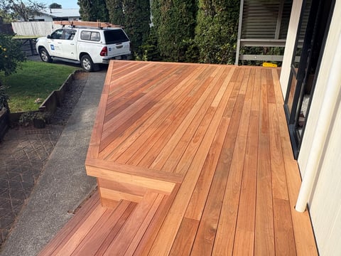 Newly stained wooden deck with warm cedar tones attached to house, white truck visible in background driveway
