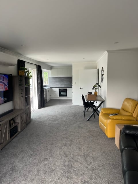 Modern open-plan apartment interior with gray carpet, white walls, kitchen, dining area, and yellow leather sofa
