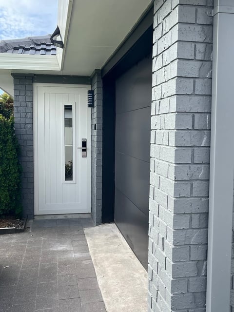 Modern home entrance with white front door, gray brick walls, and dark overhang leading to the entry porch