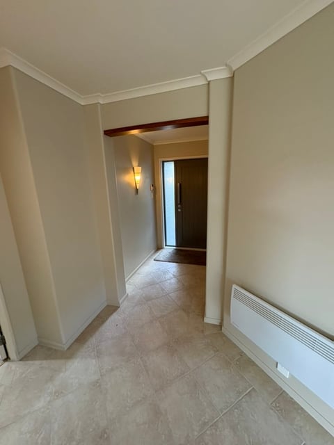 Interior hallway with beige walls, white trim, tile flooring, and white baseboard heater along the right wall