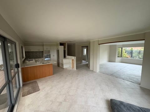 Empty modern open-plan apartment interior with light tile flooring, kitchen area, and windows overlooking greenery