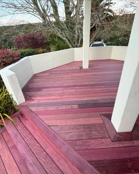 Modern deck with burgundy stained wood boards, white railings and support posts, overlooking landscaped hillside with flowering shrubs