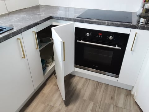 Modern kitchen corner with white cabinets, gray countertop, open dishwasher and black built-in oven, wood flooring