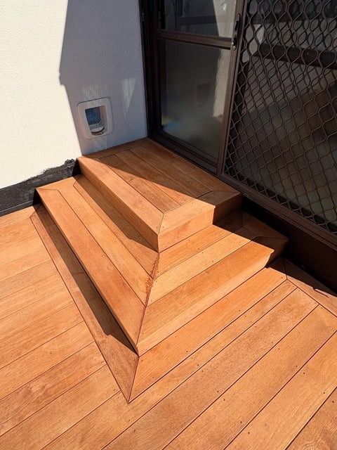 Wooden deck steps leading to an open black door with mesh screen on an RV or trailer exterior