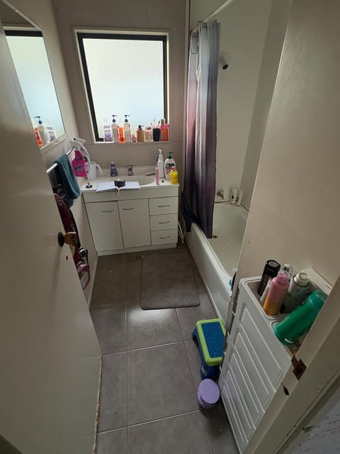 Overhead view of a narrow bathroom with a white vanity, mirror, and various toiletries and cleaning supplies organized throughout